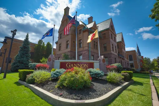 A red-stone Gannon University building behind the GANNON sign and three flags in Erie.