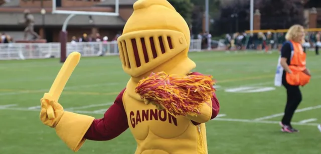 Victor, Gannon's golden-knight mascot, holding a sword and a pom-pom on the football field.